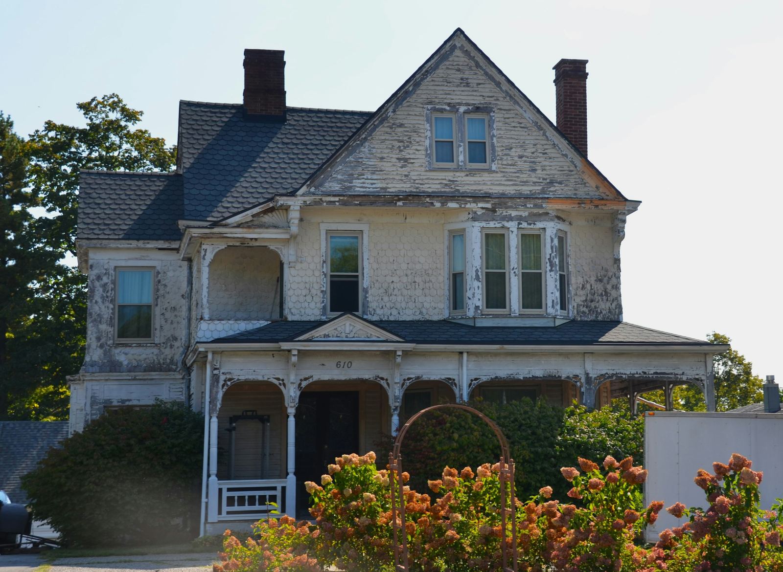 Older house with peeling paint and overgrown shrubs